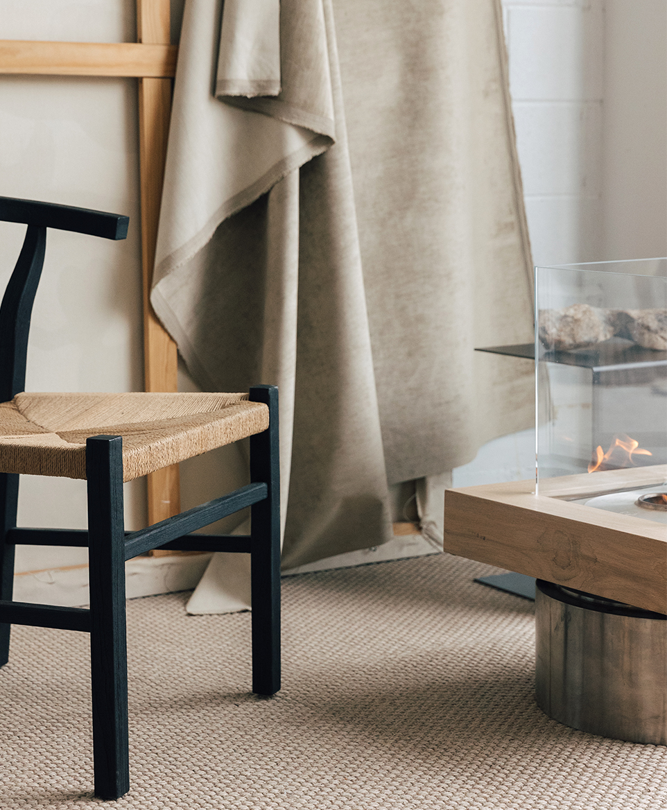 ozeano_studio silla de mimbre y madera negra y marrón con una mesa y una cortina en tonos neutros al lado